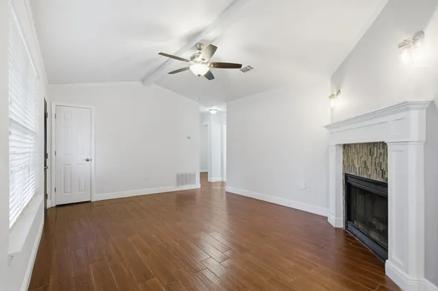 an empty room with wooden floor fireplace and windows