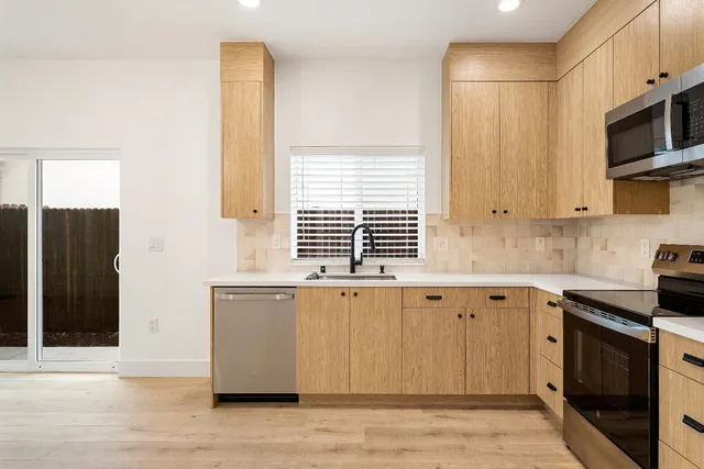 a large kitchen with granite countertop a stove a sink a refrigerator and white cabinets with wooden floor