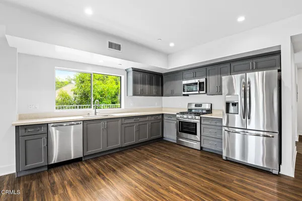 a kitchen with stainless steel appliances granite countertop a refrigerator a stove top oven a sink and dishwasher with wooden floor