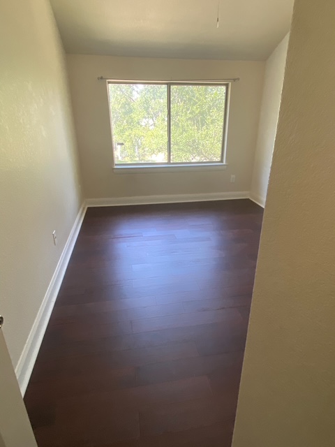 6708 Menchaca Road, Unit 25 Austin, TX 78745 - Photo 2 of 8 Rich wood flooring anchors this bedroom featuring a wide window looking out to leafy trees.
