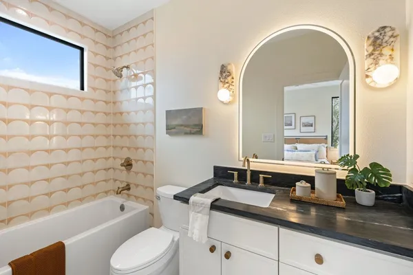 a bathroom with a granite countertop sink a toilet mirror and bathtub