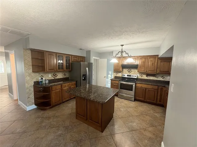 a kitchen with stainless steel appliances kitchen island granite countertop a stove refrigerator and cabinets