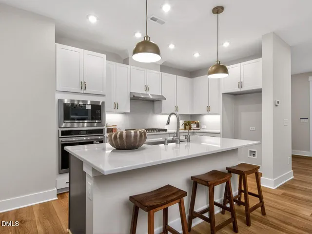 a kitchen with stainless steel appliances granite countertop a sink a stove a refrigerator and chairs