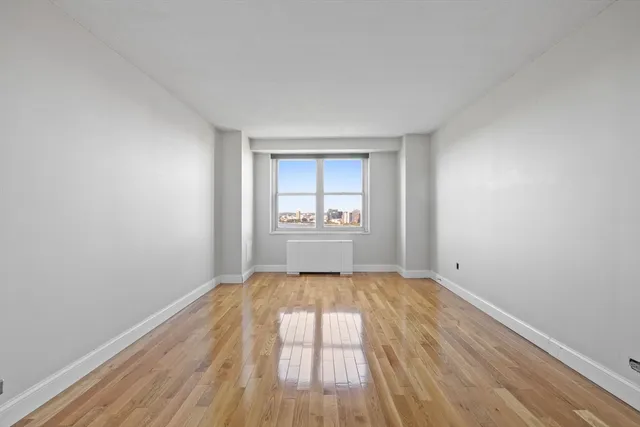 a view of an empty room with a window and wooden floor