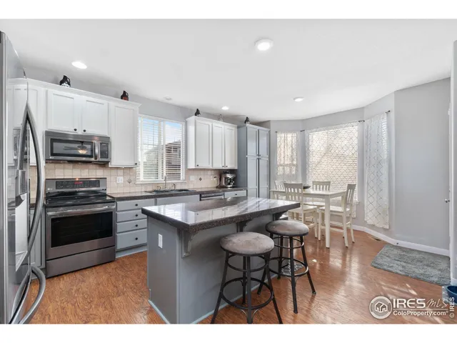 a kitchen with stainless steel appliances granite countertop a stove a sink a microwave a refrigerator and white cabinets with wooden floor