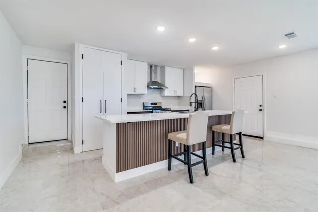 a kitchen with stainless steel appliances kitchen island granite countertop a stove a sink a refrigerator with white cabinets and couches