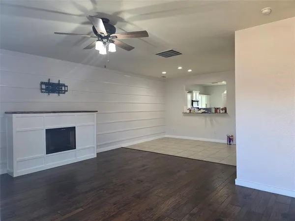 a view of an empty room with wooden floor and a kitchen