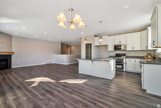 2449 Scarlet Road, Unit 249 Eagle Mountain, UT 84005 - Photo 16 of 26 Spacious room featuring wood-finish flooring, a kitchen island with pendant lighting, white cabinetry, and stainless steel appliances