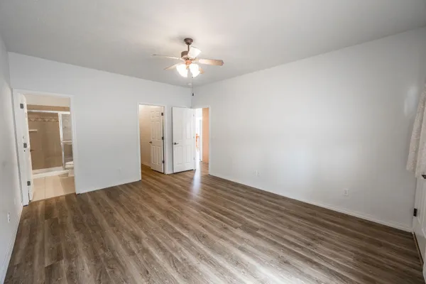 a view of an empty room with wooden floor and a ceiling fan