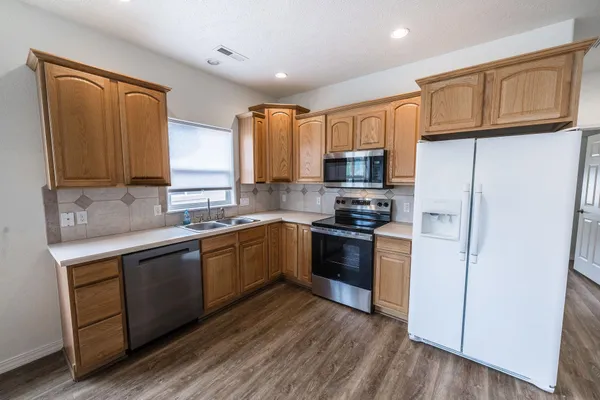 a kitchen with stainless steel appliances granite countertop a stove a sink dishwasher a refrigerator and a microwave oven with wooden floor