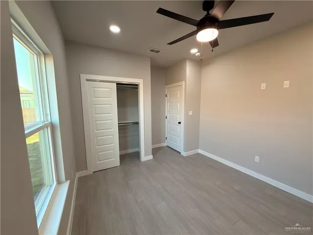 an empty room with wooden floor fan and windows