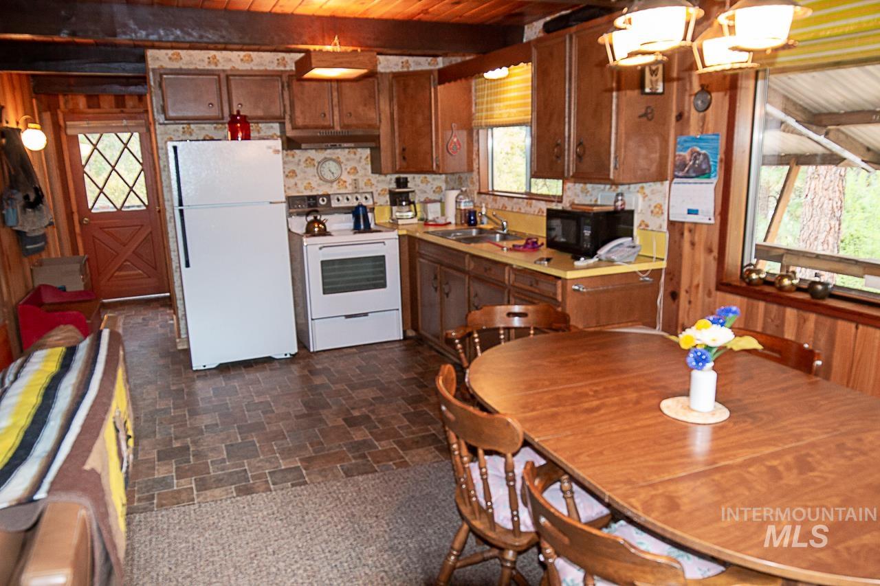 225 Mesplie Road Placerville, ID 83666 - Photo 14 of 39 Kitchen with light countertops, white appliances, a wood ceiling with exposed beams, wood walls, and brick patterned flooring