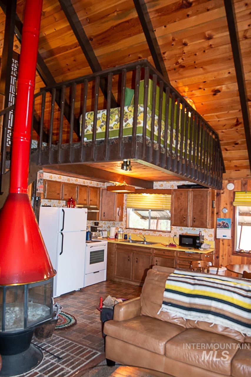225 Mesplie Road Placerville, ID 83666 - Photo 19 of 39 Living room featuring a wooden ceiling with exposed beams, wood walls, high vaulted ceiling, and a wood stove