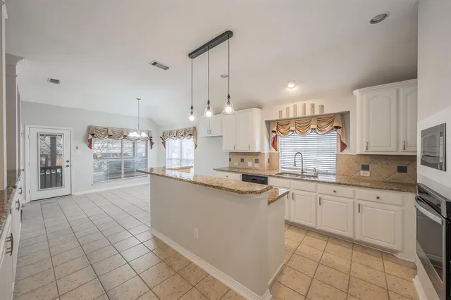 a large kitchen with granite countertop lots of white cabinets a sink and dishwasher