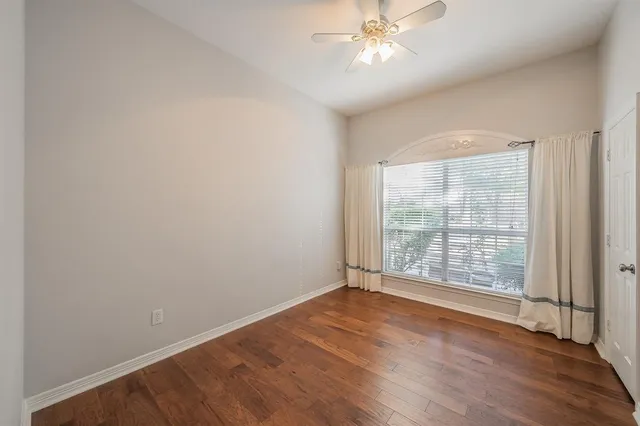 an empty room with wooden floor fan and windows