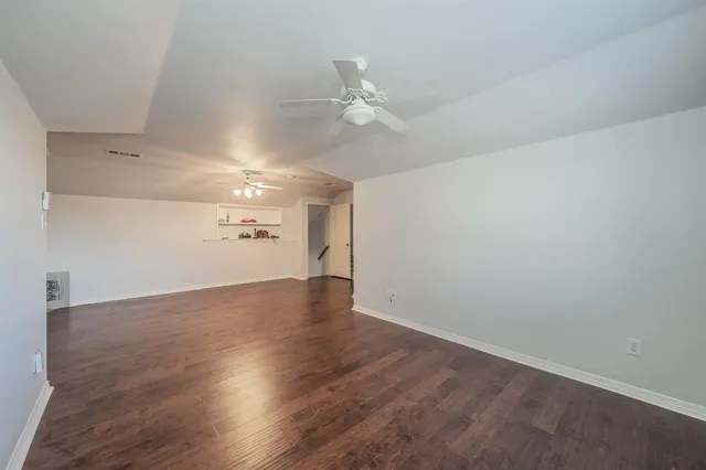an empty room with wooden floor ceiling fan and windows