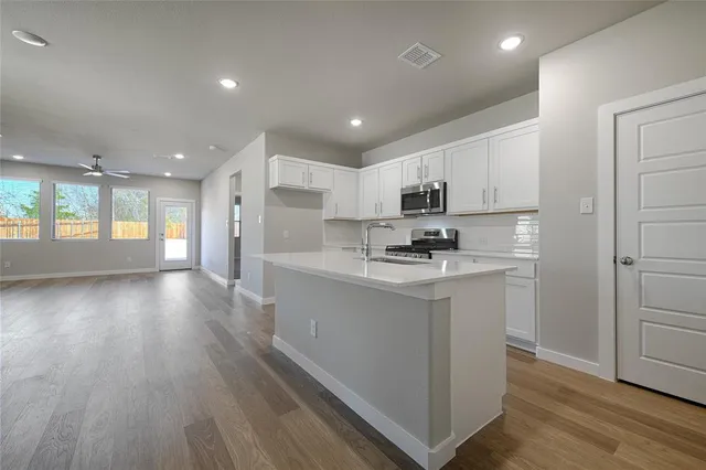 a kitchen with stainless steel appliances granite countertop a refrigerator a sink dishwasher a stove and white countertops with wooden floor