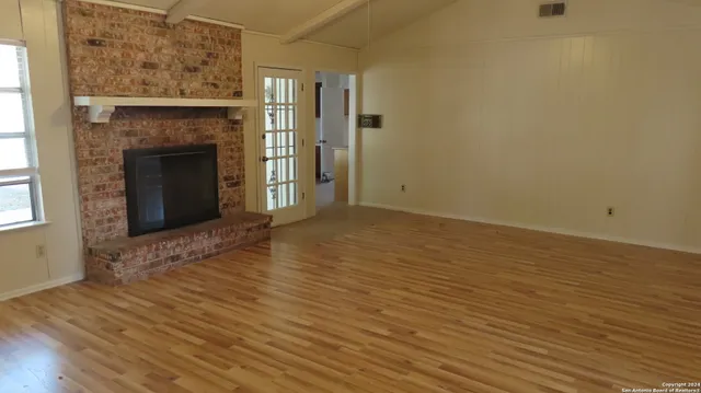 a view of an empty room with wooden floor and a fireplace