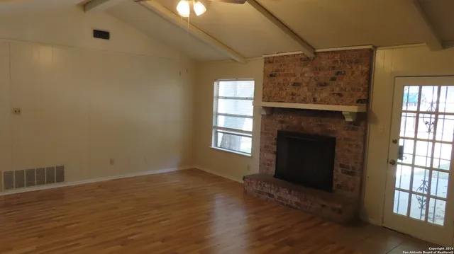 a view of an empty room with wooden floor and a window