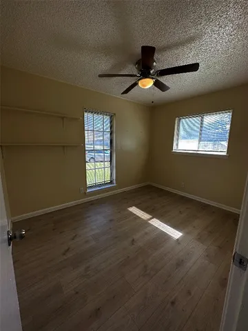 an empty room with wooden floor chandelier fan and windows