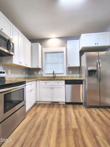 a large kitchen with granite countertop a stove top oven a sink dishwasher a refrigerator and white cabinets with wooden floor