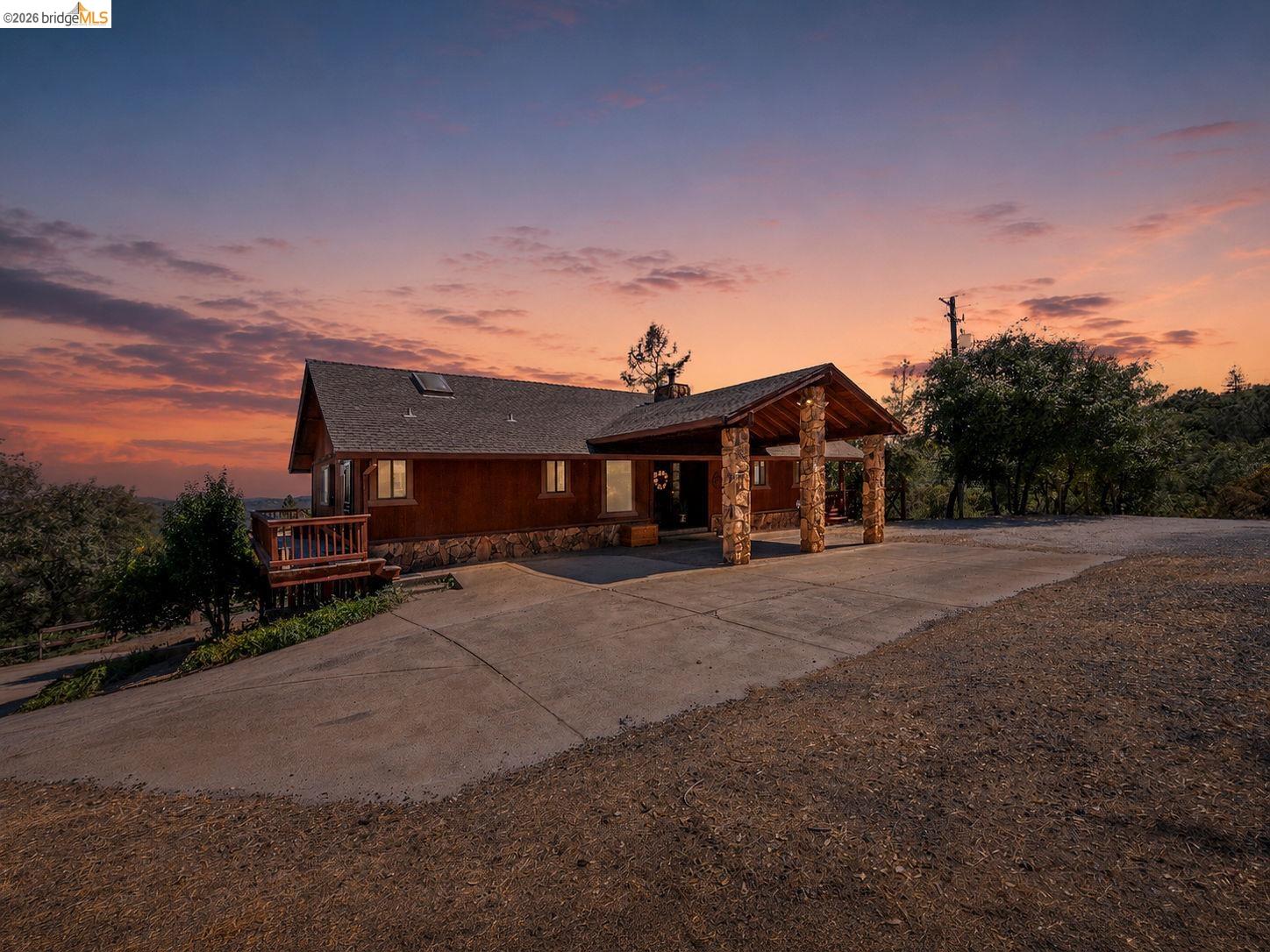 22963 Robertson Ranch Road Sonora, CA 95370 - Photo 68 of 90 Rustic-style residence featuring a dark wood exterior, a covered entryway with stone-clad pillars, a dark shingle roof, and a concrete driveway