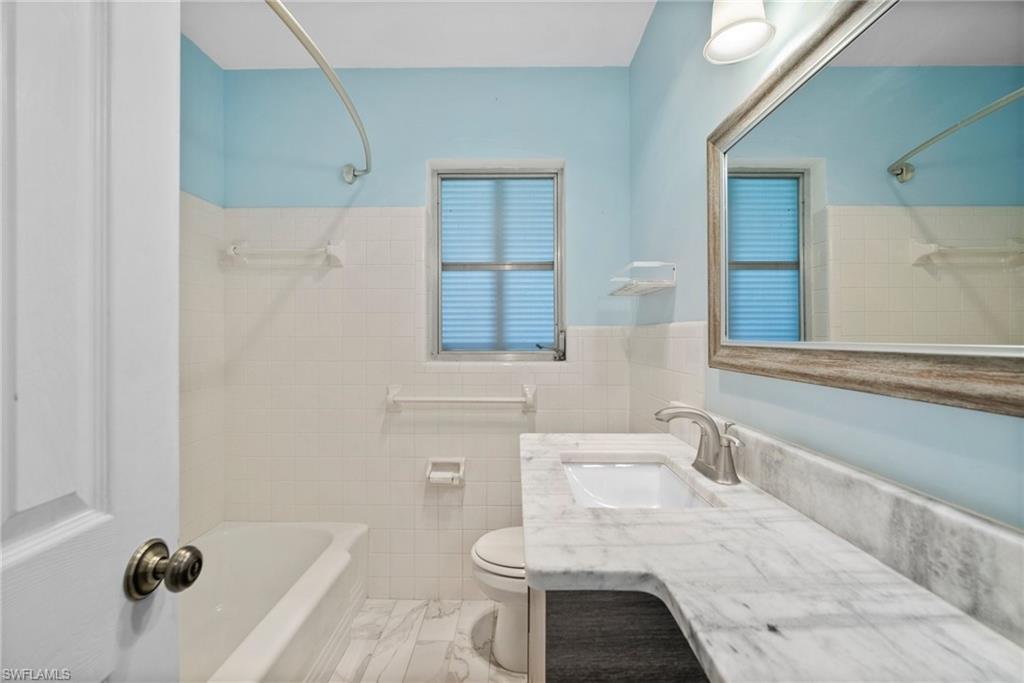 1449 Charles Road Fort Myers, FL 33919 - Photo 17 of 40 Full bathroom with tile walls, tile patterned flooring, toilet, vanity, and tiled shower / bath combo