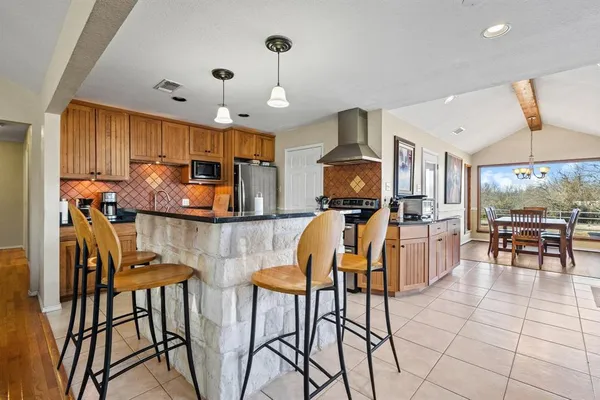 a kitchen with stainless steel appliances kitchen island granite countertop a stove a sink a dining table and chairs with the cabinets