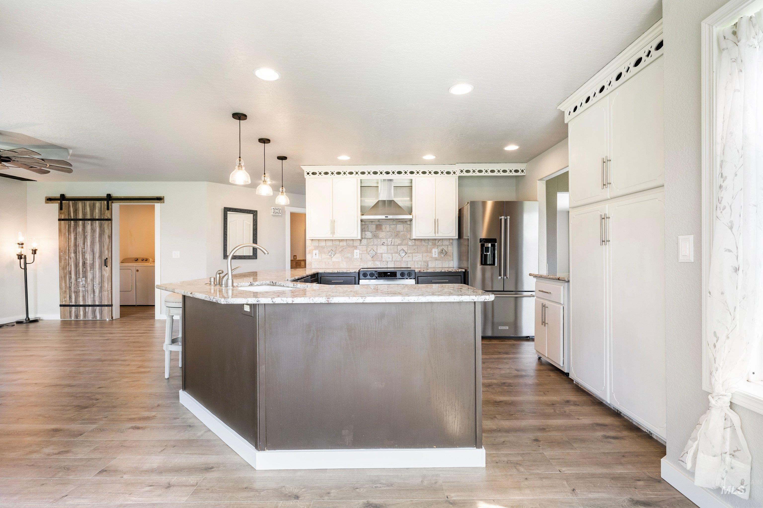 7657 Track Road Nampa, ID 83686 - Photo 15 of 49 Open-concept kitchen with a central island featuring a sink, stainless steel appliances, white cabinetry, recessed lighting, and wood-finish flooring