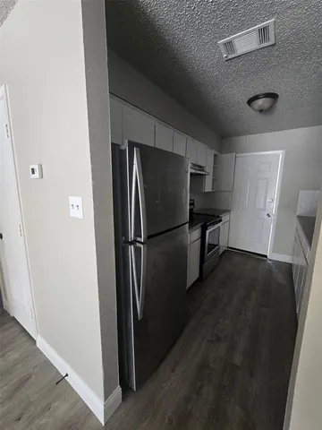 a view of a refrigerator in kitchen and an empty room with wooden floor windows