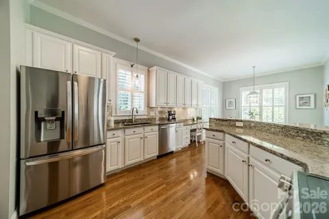 a large kitchen with a refrigerator a sink dishwasher a stove and white cabinets with wooden floor