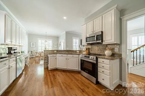 a kitchen with granite countertop a stove top oven a sink dishwasher and a refrigerator with wooden floor