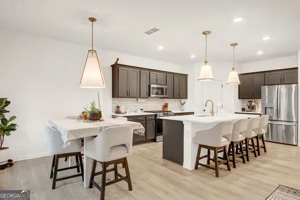 a kitchen with stainless steel appliances a dining table chairs sink and white cabinets