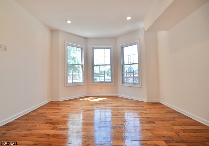 131 Sylvan Avenue Newark, NJ 07104 - Photo 5 of 9 a view of an empty room with wooden floor and a window