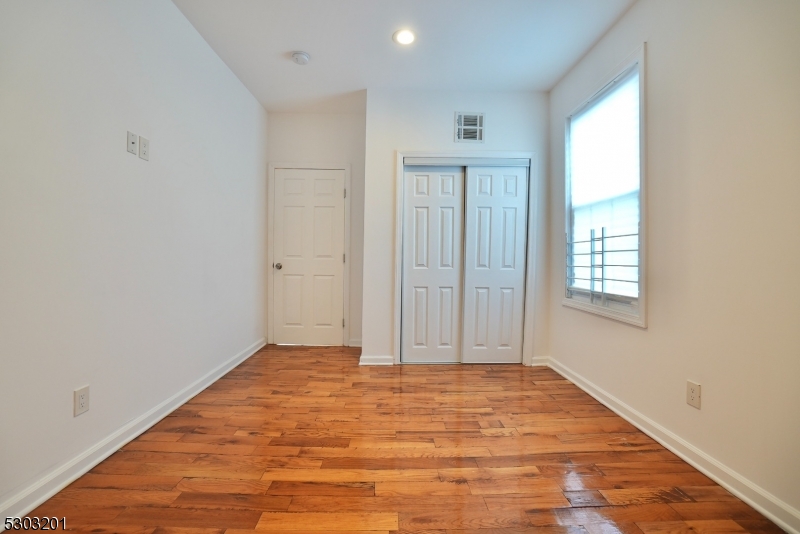 131 Sylvan Avenue Newark, NJ 07104 - Photo 7 of 9 an empty room with wooden floor and windows