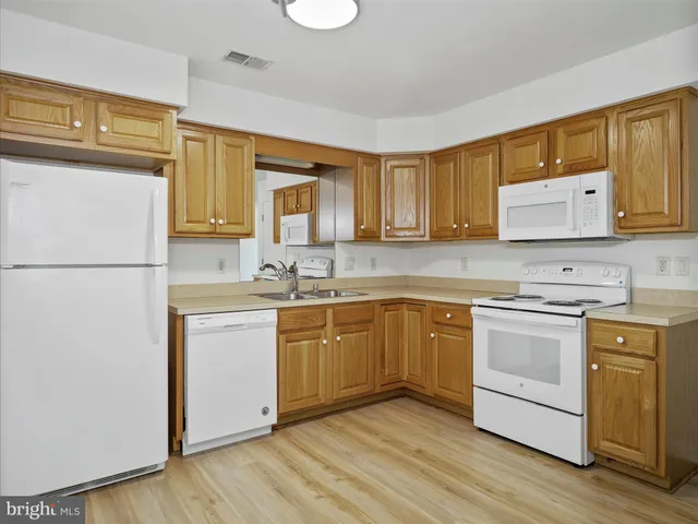 a kitchen with stainless steel appliances granite countertop a refrigerator a stove top oven and a sink with wooden floors