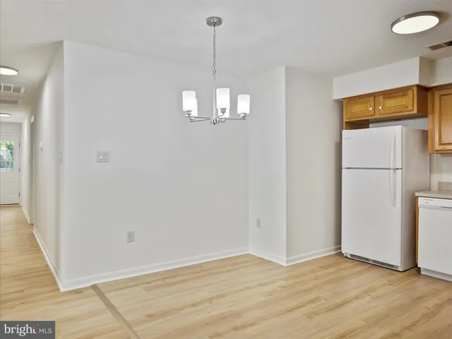 a view of a refrigerator in kitchen and an empty room with wooden floor