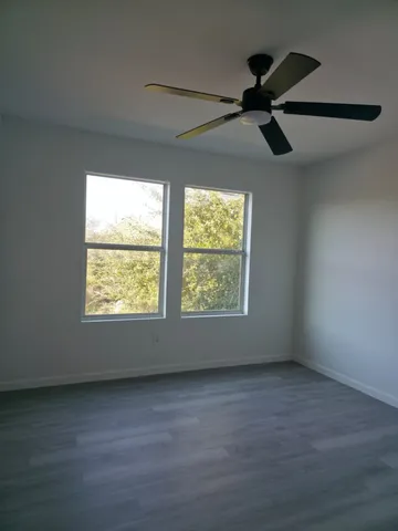 an empty room with wooden floor fan and windows