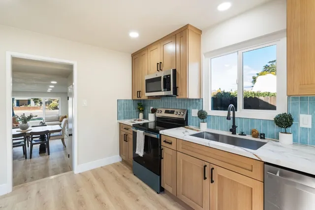 a kitchen with stainless steel appliances granite countertop a stove top oven a sink dishwasher a microwave oven and a refrigerator with wooden floor