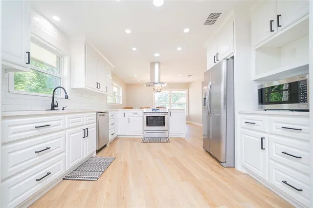 a large white kitchen with cabinets stainless steel appliances and a fireplace