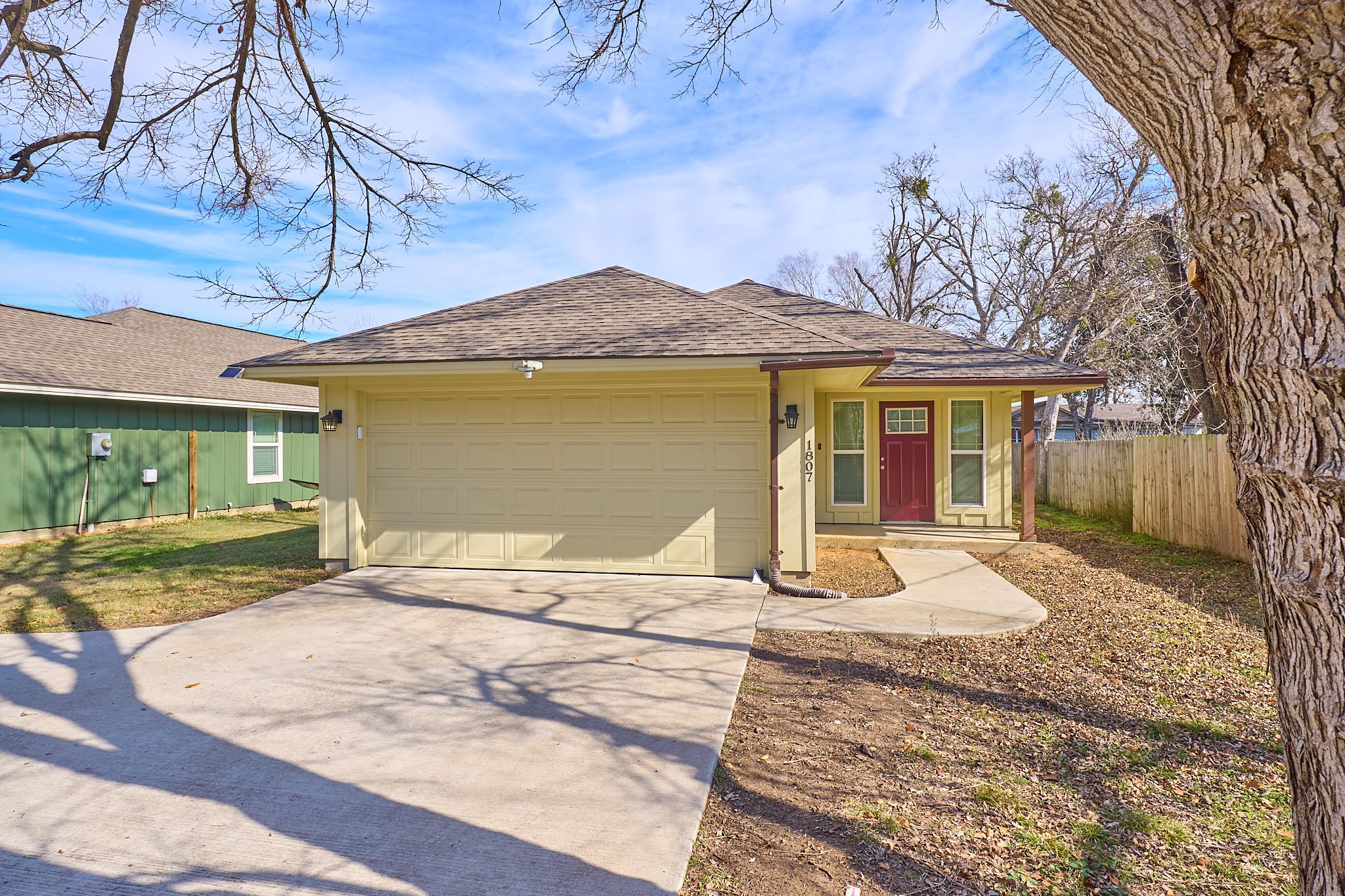 1807 Nuches Lane Bryan, TX 77803 - Photo 27 of 27 Charming single-story home with a two-car garage, featuring a welcoming red front door and a spacious driveway. The yard is partially shaded with mature trees and a fenced backyard, offering privacy and outdoor space.