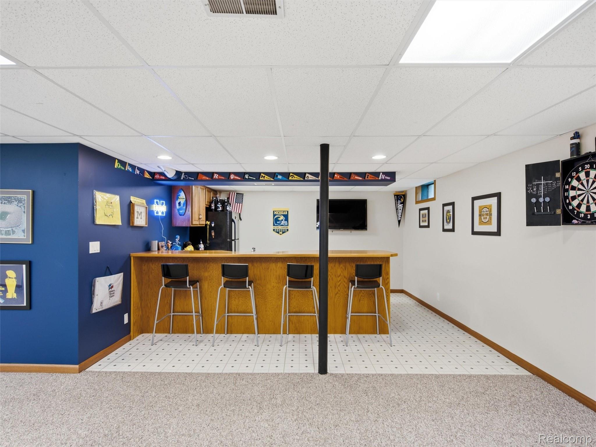 5003 Mason Road Howell, MI 48843 - Photo 30 of 59 Finished lower level featuring a built-in bar with light wood-finish cabinetry, a drop ceiling with recessed lighting and fluorescent fixtures, a dedicated dartboard area, and a television mounting space