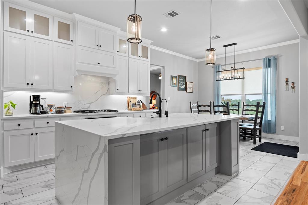 1024 Henry Way Springtown, TX 76082 - Photo 1 of 29 Spacious kitchen featuring an expansive island with a waterfall countertop, white shaker-style cabinetry, and a matching stone backsplash