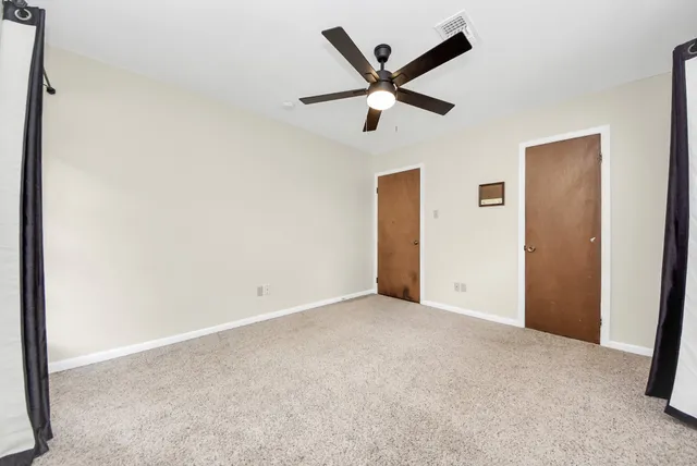 an empty room with ceiling fan and windows