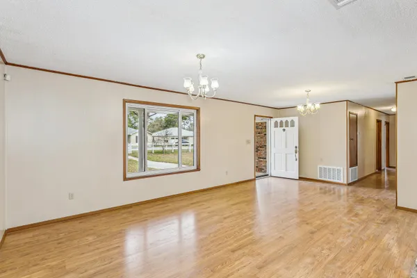 an empty room with wooden floor chandelier and windows