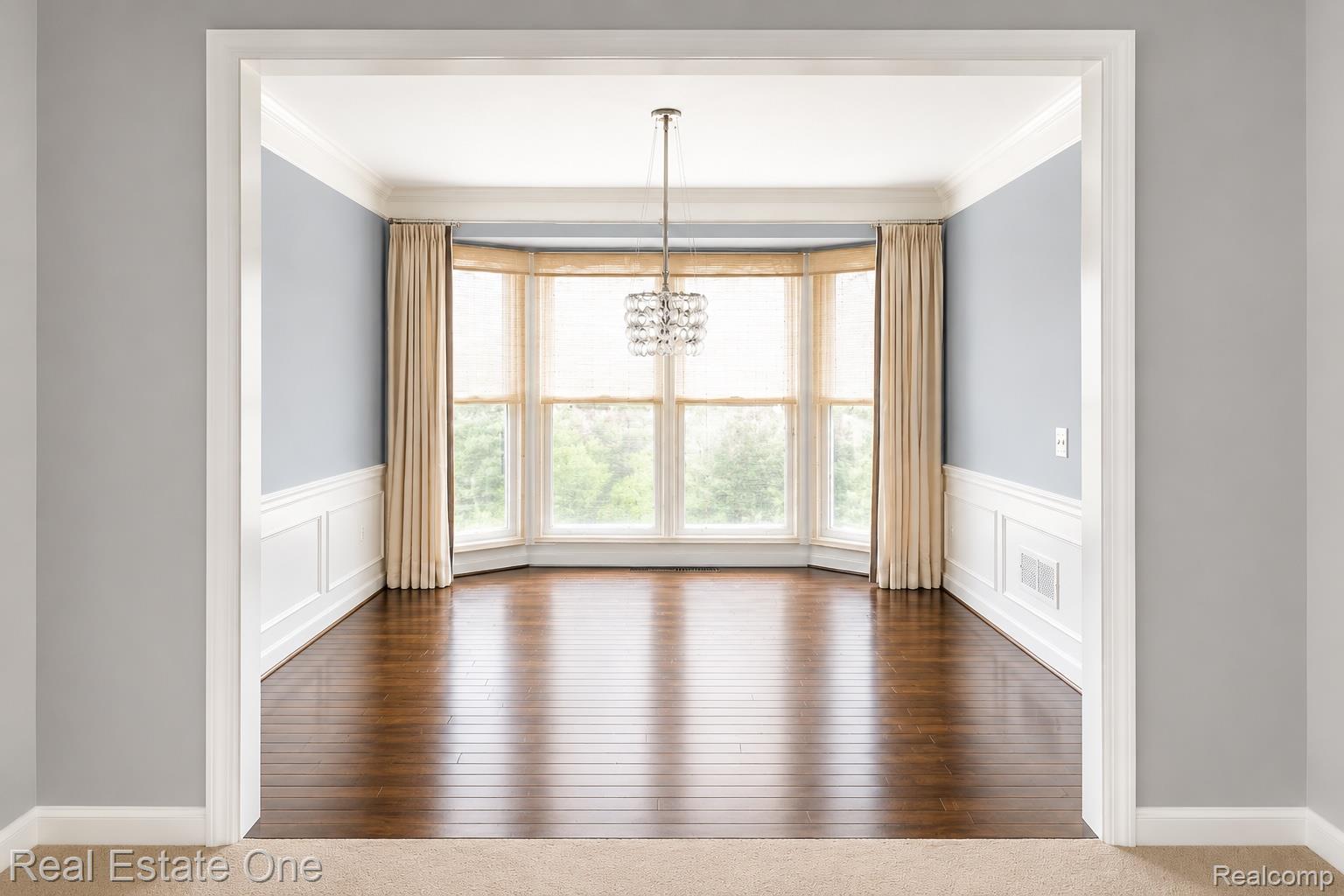 1141 Sandy Ridge Drive Rochester, MI 48306 - Photo 4 of 9 Expansive room with a bay window, hardwood flooring, wainscoting, crown molding, and a decorative chandelier