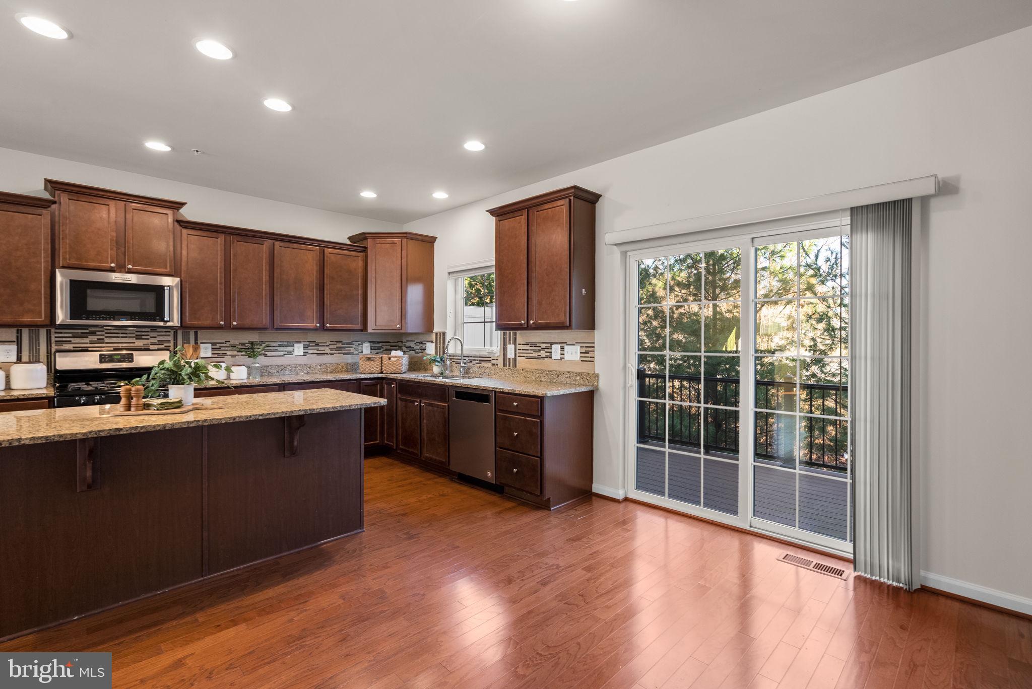 8012 Alchemy Way Elkridge, MD 21075 - Photo 12 of 46 a kitchen with stainless steel appliances granite countertop a stove top oven a sink dishwasher a refrigerator and a microwave oven with wooden floor
