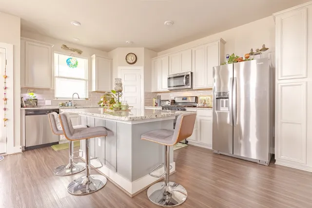 a kitchen with stainless steel appliances granite countertop a refrigerator a stove top oven and a dining table with wooden floor