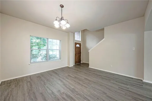 an empty room with wooden floor chandelier and windows