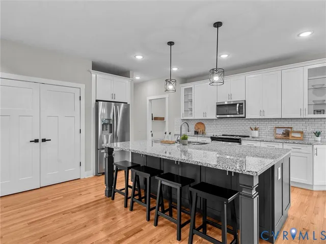 a kitchen with stainless steel appliances granite countertop a stove a refrigerator a kitchen island a sink and chairs with wooden floor